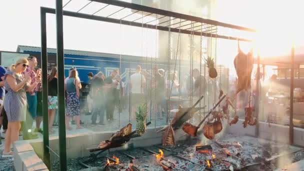 Rusland, Sint-Petersburg, 18 augustus 2019: Grote stukken varkensvlees, rundvlees en ananasvlees worden gekookt op een enorme grill, brandende houtblokken op een ijzeren plaat als kolen, de varkenskop wordt gebakken op een open vuur. — Stockvideo