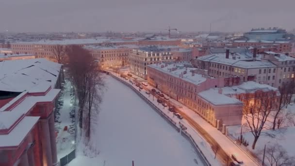 Luftaufnahme der Böschung des zugefrorenen Griboedov-Kanals an einem verschneiten Winterabend, nächtliche Beleuchtung von Gebäuden und Straßen, nächtliches Stadtbild — Stockvideo