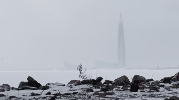 Rússia, São Petersburgo, 22 de janeiro de 2022: O arranha-céu centro de Lakhta pela companhia de petróleo Gazprom na tempestade de neve em um fundo, nevasca, costa rochosa do Golfo da Finlândia em primeiro plano — Vídeo de Stock
