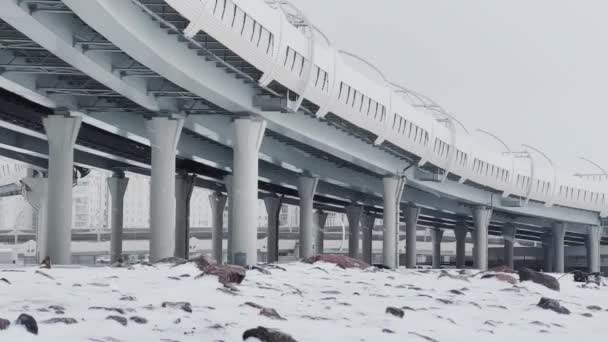 Piliers sous une route à grande vitesse un jour d'hiver, un pont suspendu par câble dans la brume neigeuse en arrière-plan, personne — Video