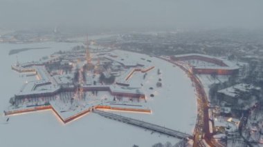 Bir kış akşamı kar fırtınasında Peter ve Paul Kalesi 'nin hava görüntüleri, gece aydınlatması Petropavlos Katedrali altın ışıkla parıldıyor, arka planda St. Petersburg manzarası var.
