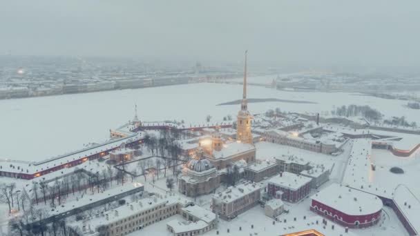 冬の夜、雪の嵐の中でピーターとポール要塞の空中映像、夜の照明、ペトロパヴロス大聖堂は金色の光で輝き、背景にサンクトペテルブルクの観光スポット — ストック動画