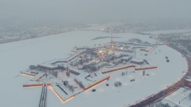 Zdjęcia lotnicze twierdzy Piotra i Pawła podczas burzy śnieżnej w zimowy wieczór, oświetlenie nocne, katedra Petropavlos świeci złotym światłem, zabytki Sankt Petersburga w tle — Wideo stockowe