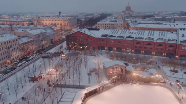 Karlı bir kış akşamında New Holland parkının hava manzarası, binaların ve sokakların gece aydınlanması, gece şehir manzarası, açık hava buz pateni pisti, arka planda St. Petersburg 'un simgeleri. — Stok video