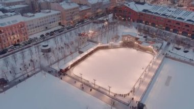 Karlı bir kış akşamında New Holland parkının hava manzarası, binaların ve sokakların gece aydınlanması, gece şehir manzarası, açık hava buz pateni pisti, arka planda St. Petersburg 'un simgeleri. 