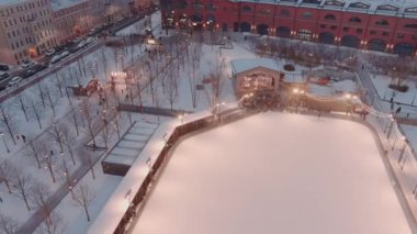 Karlı bir kış akşamında New Holland parkında, açık hava buz pateni pisti manzarası binaların ve sokakların gece aydınlanması, gece manzarası, arka planda St. Petersburg 'un simgeleri. 