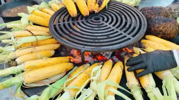 Op een grote grill worden verse maïs en ananas buiten gebakken, maïskolven worden gesponnen om zelfs te koken, een vakantie voor een groot aantal mensen — Stockvideo