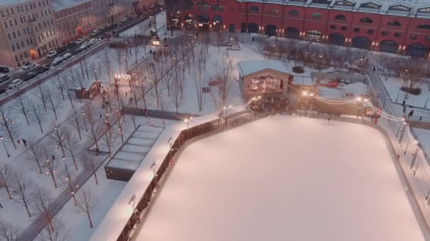 Aerial view of outdoor skating rink, in the New Holland park in a snowy winter evening, night illumination of buildings and streets, night cityscape, landmarks of St. Petersburg on a background — Stock Video