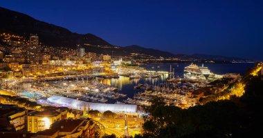 Monako 'daki Herkül limanının hava görüntüsü - Monte-Carlo alacakaranlıkta, bir sürü yat ve tekne marinada demirli, gece aydınlatmalı şehir manzarası, su, dağ ve Akdeniz' e sihirli yansıması