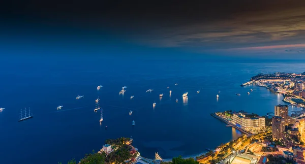 Una gran cantidad de yates y barcos a motor con iluminación nocturna están amarrados en el mar Mediterráneo, vista aérea de la bahía de Mónaco Monte Carlo al atardecer, paisaje urbano con iluminación nocturna — Foto de Stock