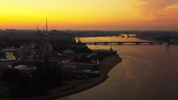 Lot dronem nad rzeką Nevą do twierdzy Piotra i Pawła o wschodzie słońca, odbicie pomarańczowego nieba na wodzie, zwodzone mosty Trocki i Liteiny są rozdzielone, — Wideo stockowe