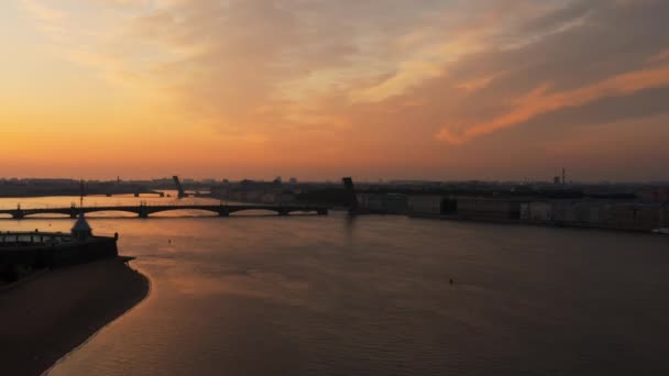 Lot dronem nad rzeką Nevą do wzniesionego mostu zwodzonego Trójca o wschodzie słońca, okręt wojenny przechodzi pod mostem, próba parady statku, odbicie pomarańczowego nieba, zwodzone mosty Trocki i Liteiny — Wideo stockowe