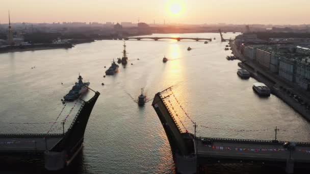 Krajobraz powietrzny z okrętami wojennymi w rzece Neva przed świętem rosyjskiej marynarki wojennej wczesnym rankiem, okręty wojenne przechodzą pod podniesionym mostem zwodzonym, najnowsze krążowniki wśród zabytków, most pałacowy — Wideo stockowe