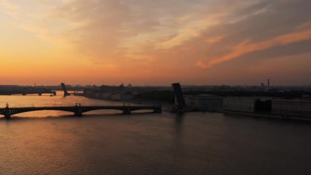 Drohnenflug über die Newa zu einer erhöhten Zugbrücke Trinity bei Sonnenaufgang, Kriegsschiff fährt unter der Brücke durch, Schiffsparadeprobe, Spiegelung des orangen Himmels, Zugbrücken Troitsky und Liteiny — Stockvideo