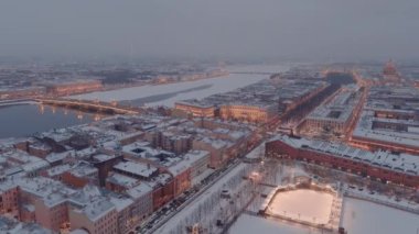 Karlı bir kış akşamında St. Petersburg 'un dönüm noktalarını gösteren hava aracı manzarası, New Holland adası, binaların gece aydınlığı şehir manzarası, açık hava buz pateni pisti.