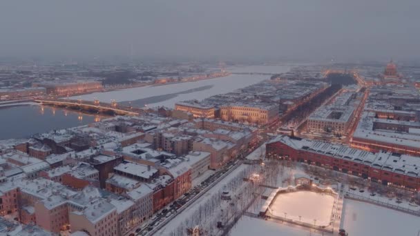 Karlı bir kış akşamında St. Petersburg 'un dönüm noktalarını gösteren hava aracı manzarası, New Holland adası, binaların gece aydınlığı şehir manzarası, açık hava buz pateni pisti. — Stok video