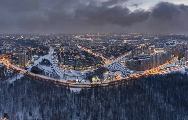 Aerial winter cityscape of St. Petersburg - Russia at dusk, drone flies over huge housing estates and public park, construction cranes, night illumination, clouds float below drone — Stock Photo, Image