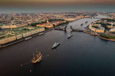 Sabahın erken saatlerinde Rus donanmasının bayramından önce Neva Nehri 'ndeki savaş gemileriyle hava manzarası yükseltilmiş bir asma köprünün altından geçen savaş gemileri, saray köprüsünün en son kruvazörleri.