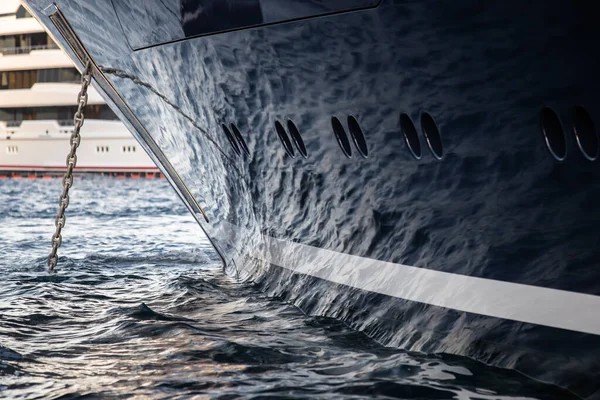 The mesmerizing reflection of the water on the glossy side of a huge yacht anchored, chrome details, chains and ropes to the muring descend into the water — Stock Photo, Image