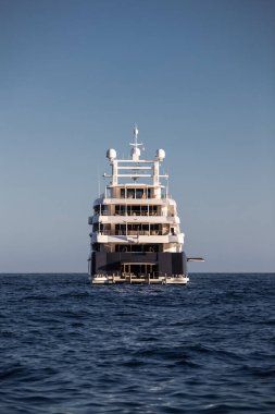 Güneşli bir günde denizde büyük bir yatın kıç tarafı, motorlu teknenin parlak tahtaları, krom kaplama tırabzanlar, limana demirlemiş megayacht, parlak tahtaya güneş yansıması