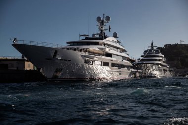 Günbatımında Monaco limanında iki büyük yat, motorlu teknenin parlak tahtaları, krom kaplama tırabzanlar, marinada demirli megayacht, parlak tahtada güneş yansıması, arka planda dağ