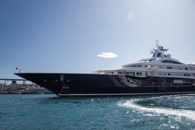 Güneşli bir günde Monaco limanında büyük bir yatın sol panosu, motorlu teknenin koyu mavisi, krom kaplama tırabzan, marinada demirli, parlak tahtada güneş yansıması.
