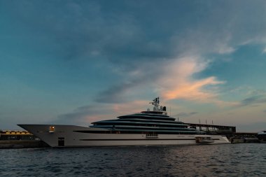 Günbatımında Monaco Limanı 'nda büyük bir yatın sol tarafı, motorlu teknenin parlak panosu, krom kaplı korkuluk, megayacht marinada demirli, pembe gökyüzü, alacakaranlık