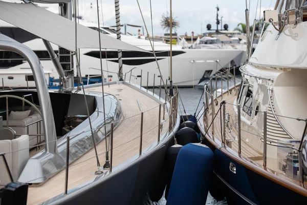 wooden decks of sailing yachts in classic style with chrome railings along the edge of the boats in Monaco at sunny day, hangs a lot of fenders, a huge yacht in the background