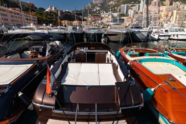 Güneşli bir günde Monako limanında bir sürü motorlu tekne var, Monte Carlo, arka planda dağ, renkli iç kısımlar, marinada demirli, parlak tahta üzerinde güneş yansıması.