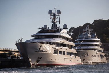 İki büyük yat gün batımında Monako limanında, güneş yansıması motorlu teknelerin parlak tahtalarında, krom kaplı tırabzanlar, Megayacht marinada demirli, dağ arka planda