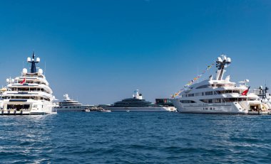 Güneşli bir günde Monako limanında bir sürü büyük yat vardır, Monte Carlo, arka planda dağ, motorlu teknenin parlak tahtaları, marinada demirli megayachtlar, parlak tahtada güneş yansıması.