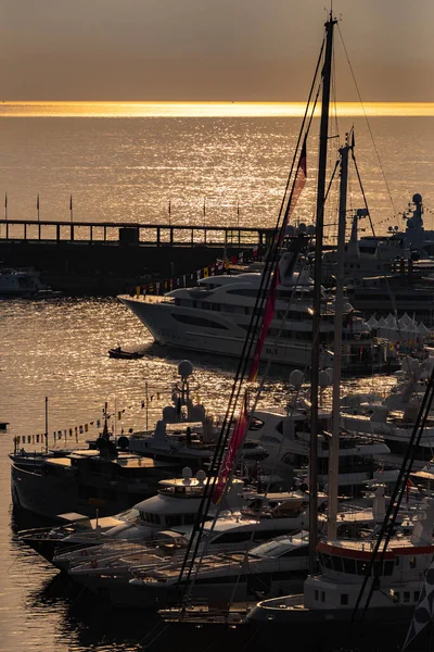 Много огромных яхт в порту Монако на рассвете, глянцевая доска моторной лодки, хромированные перила, мегаяхты пришвартованы в марине, солнечные отражения, водная поверхность на заднем плане — стоковое фото