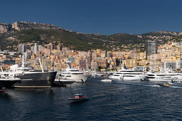 A lot of huge yachts are in port of Monaco at sunny day, megayachts are moored in marina, is a yacht show, Monte Carlo, real estate housing is on background, glossy board of the motor boat — Stock Photo, Image