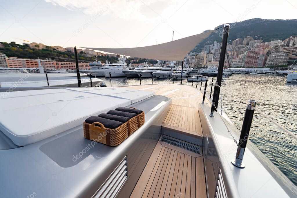 The front deck of huge yacht in port of Monaco at sunset, the place for landing of helicopter, a lot of motorboats are on background, the chrome plated handrail, megayacht is moored in marina, dusk