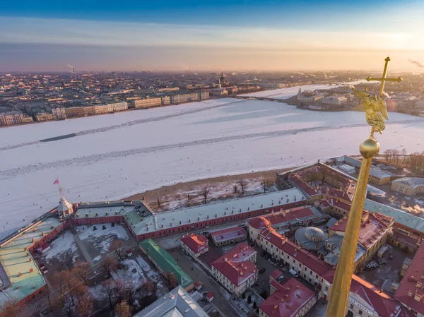 Αεροφωτογραφία του χρυσού αγγέλου και Σταυρού σε ακίδα του καθεδρικού ναού του Πέτρου και Παύλου στην Αγία Πετρούπολη το ηλιοβασίλεμα, κατεψυγμένα Neva ποταμού, ηλιόλουστη παγωμένη ημέρα, Χειμερινό Παλάτι, Ναυαρχείο, Αστρικές στήλες — Φωτογραφία Αρχείου