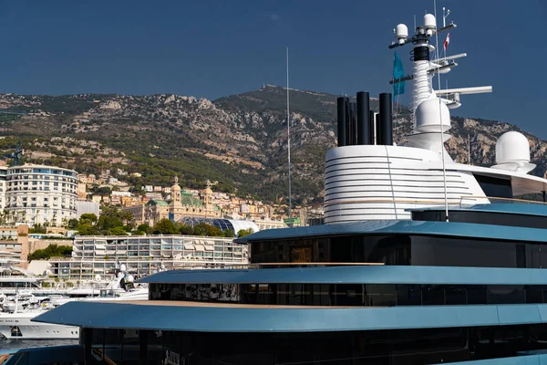 Památky Monaka přes paluby obrovské jachty modré barvy v přístavu Hercule v slunečný den, lesklá deska motorového člunu, odraz slunce na lesklé palubě, hory jsou na pozadí — Stock fotografie