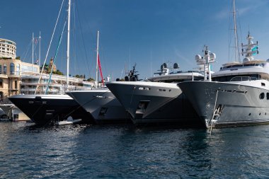 Güneşli bir günde Monako limanında bir sürü büyük yat vardır, Monte Carlo, arka planda dağ, motorlu teknenin parlak tahtaları, marinada demirli megayachtlar, parlak tahtada güneş yansıması.