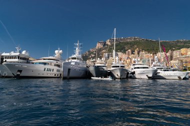 Güneşli bir günde Monako limanında bir sürü büyük yat vardır, Monte Carlo, arka planda dağ, motorlu teknenin parlak tahtaları, marinada demirli megayachtlar, parlak tahtada güneş yansıması.