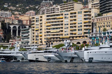 Güneşli bir günde Monako limanında bir sürü büyük yat var, megayachtlar marinada demirli, bir yat şovu, Monte Carlo, emlak konutları arka planda, motorlu teknenin parlak kurulu.