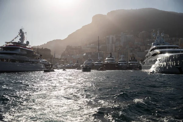 Una gran cantidad de enormes yates están en el puerto de Hercule de Mónaco al atardecer, la montaña está en el fondo, la luz de fondo mágica está en las tablas brillantes de los barcos a motor, megayates están amarrados en el puerto deportivo, reflejos del sol — Foto de Stock