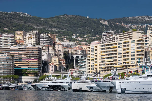 A lot of huge yachts are in port of Monaco at sunny day, megayachts are moored in marina, is a yacht show, Monte Carlo, real estate housing is on background, glossy board of the motor boat — Stock Photo, Image