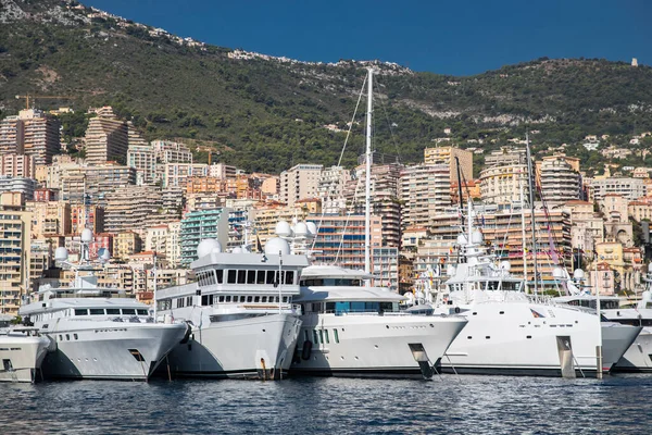 Una gran cantidad de yates enormes están en el puerto de Mónaco en el día soleado, megayates están amarrados en el puerto deportivo, es un espectáculo de yates, Monte Carlo, la vivienda de bienes raíces está en el fondo, tablero brillante de la lancha a motor — Foto de Stock