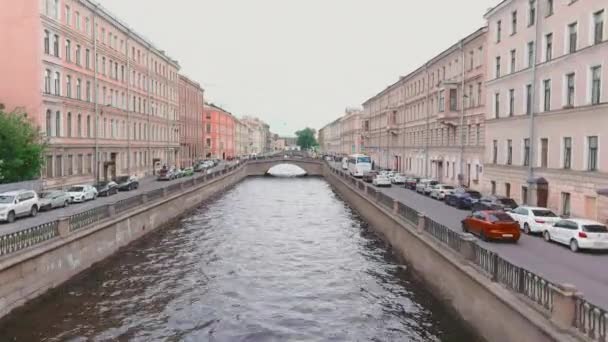 Oroszország, Szentpétervár, 2021. június 13.: Egy drón repül át a Griboyedov-csatornán egy felhős nyári napon, az emberek végigsétálnak a töltésen és a hidakon, az autók lassan mozognak és dugókban állnak — Stock videók