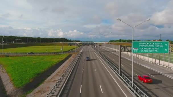 Dron přeletí vysokorychlostní dálnici za slunečného večera, auta a náklaďáky, směrové značky, zelené trávníky, dramatické mraky — Stock video