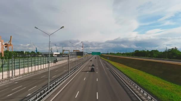 Drone voa sobre a estrada de alta velocidade em uma noite ensolarada, carros e caminhões, sinais de direção, gramados verdes, nuvens dramáticas — Vídeo de Stock