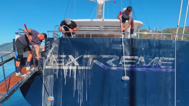 Туреччина, Мармаріс, 27 листопада 2019: Екіпаж величезного човна миє вітрильну яхту в ясну сонячну погоду, хлопці заливають воду зі шлангу і тонусу спеціальними матрацами, це готує розкішний човен. — стокове відео