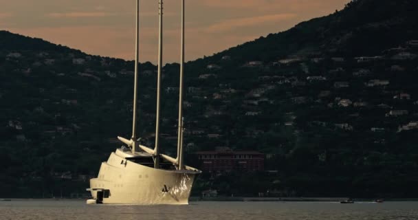 El lapso de tiempo de un enorme yate de vela con tres mástiles se encuentra en la bahía de St. Tropez al atardecer, es el sur de Francia, el yate gira alrededor de su ancla, barcos pequeños navegan casi, una pendiente, reflejos mágicos — Vídeo de stock