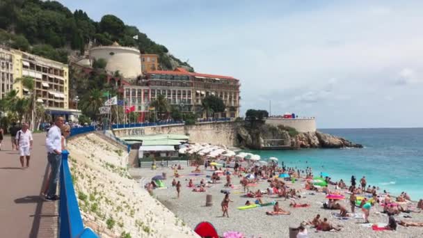 Frankrike, Nice, 21 juli 2018: Många människor på stranden på en klar solig dag, turkost vatten, parasoller från solen, en lokal attraktion - Promenade des Anglais — Stockvideo