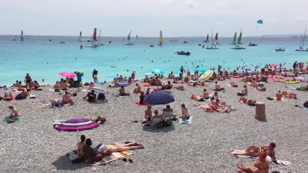 Frankrike, Nice, 21 juli 2018: Många människor på stranden på en klar solig dag, turkost vatten, parasoller från solen, en lokal attraktion - Promenade des Anglais — Stockvideo