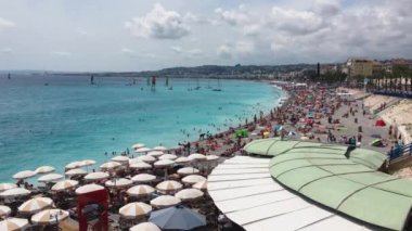 Nice 'in ana plajında bir sürü insan güneşli bir günde Fransa' da turkuaz su, güneş şemsiyeleri, yerel bir eğlence - Gezinti güvertesi des Anglais, ufukta yelkenli gemiler.